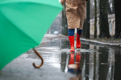 Woman in rubber boots running after umbrella outdoors on rainy day, closeup