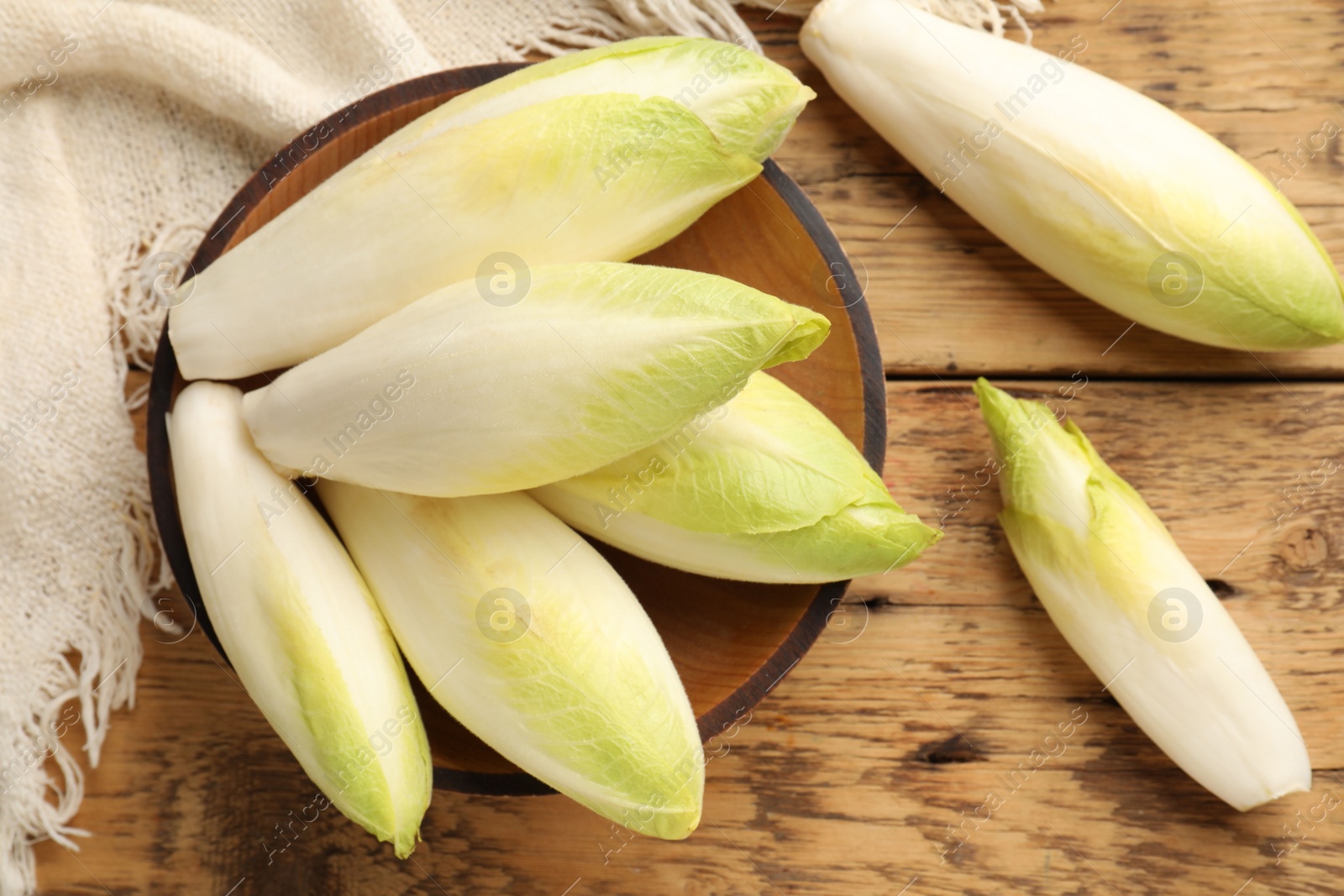 Photo of Fresh raw Belgian endives (chicory) and bowl on wooden table, top view