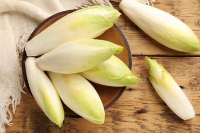 Photo of Fresh raw Belgian endives (chicory) and bowl on wooden table, top view