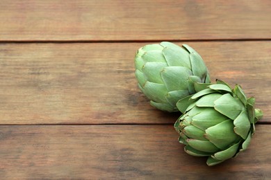 Photo of Fresh raw artichokes on wooden table. Space for text