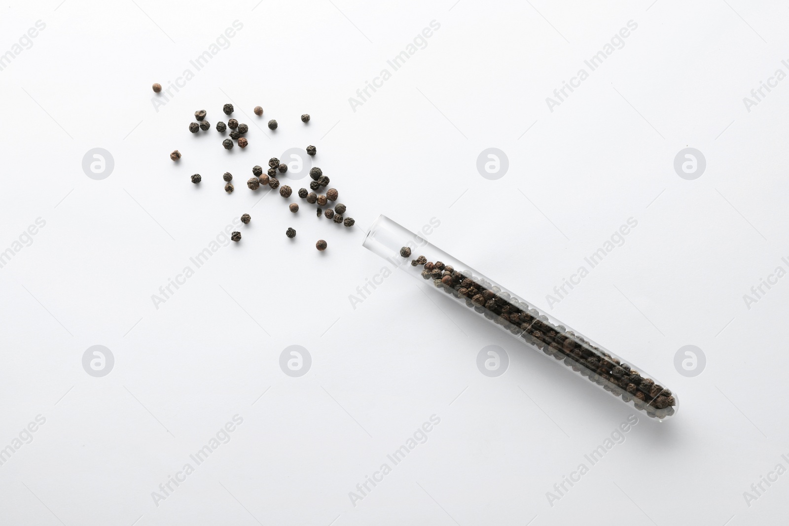 Photo of Glass tube with peppercorns on white background, top view