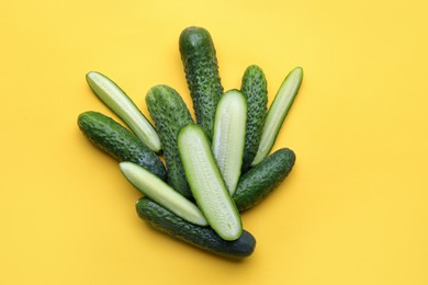 Photo of Whole and cut fresh cucumbers on yellow background, flat lay