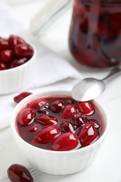 Delicious dogwood jam with berries and spoon on white wooden table, closeup