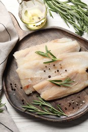 Raw cod fish, rosemary, oil and spices on white wooden table, flat lay