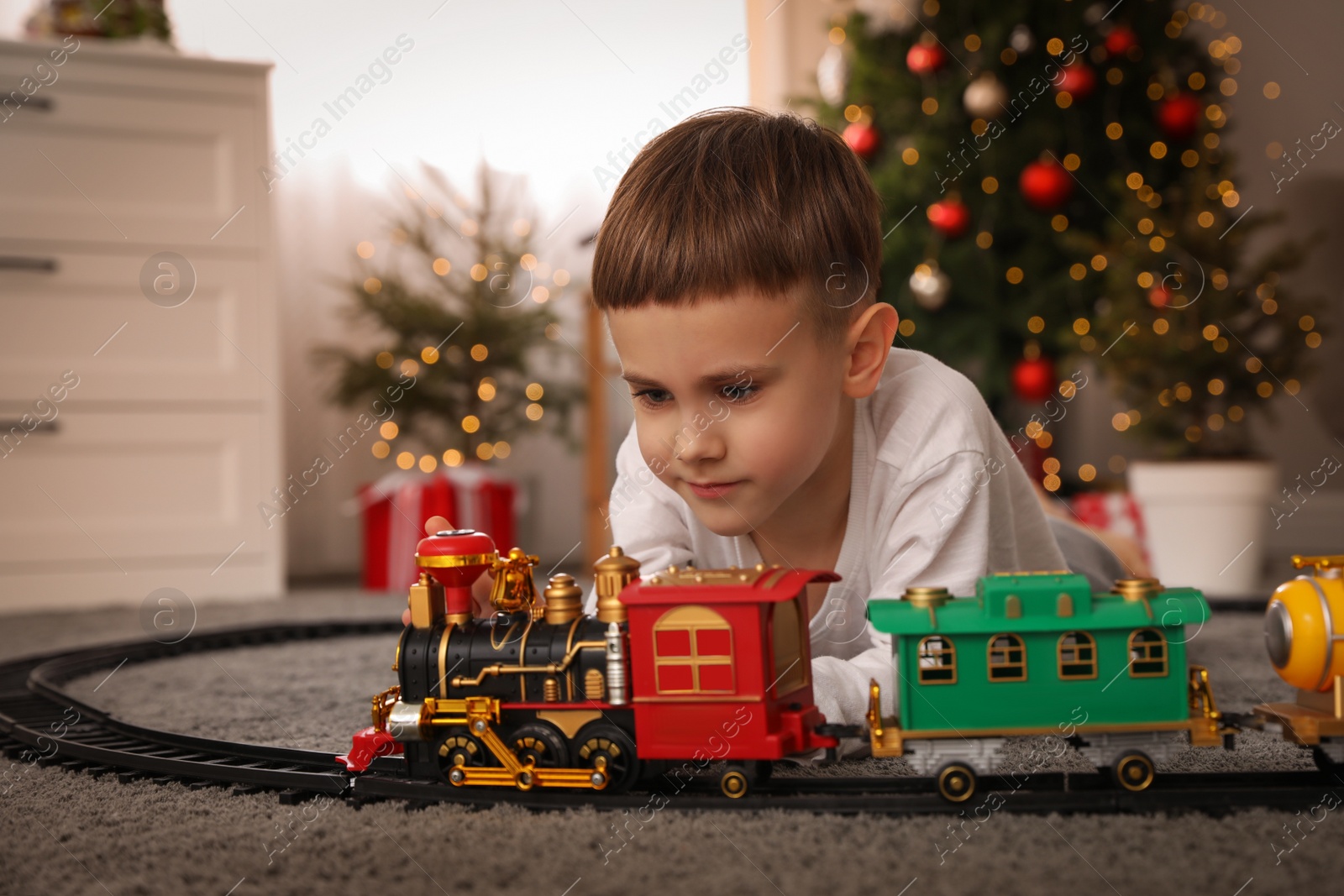 Photo of Little boy playing with colorful train toy in room decorated for Christmas