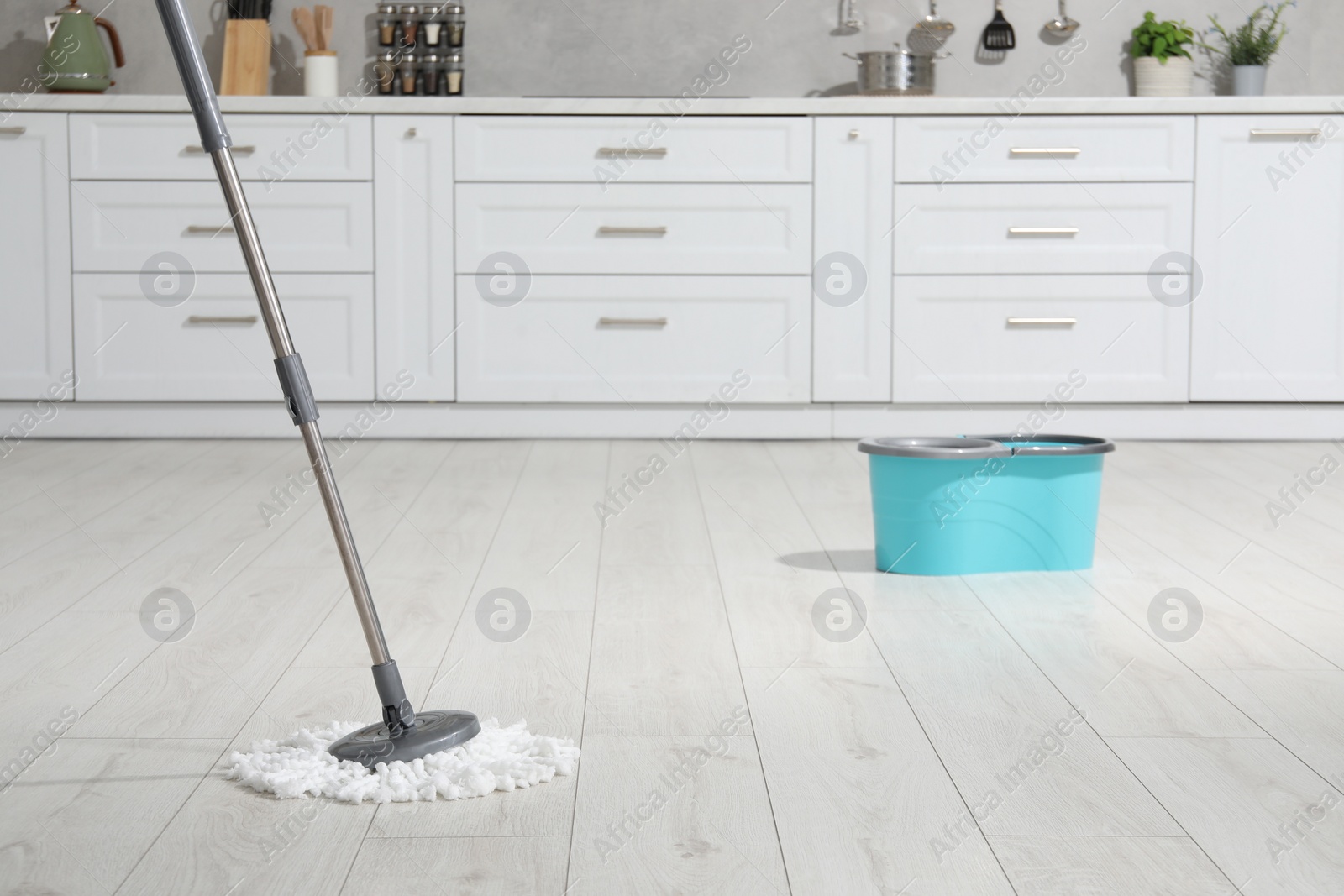 Photo of Mop and bucket on white parquet in kitchen. Cleaning floor