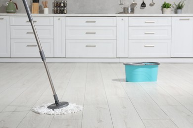 Mop and bucket on white parquet in kitchen. Cleaning floor