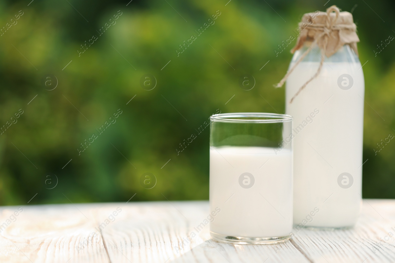 Photo of Bottle and glass of tasty fresh milk on white wooden table against blurred background, space for text