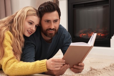 Photo of Lovely couple reading book near fireplace at home