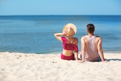 Happy young couple sitting together at beach on sunny day