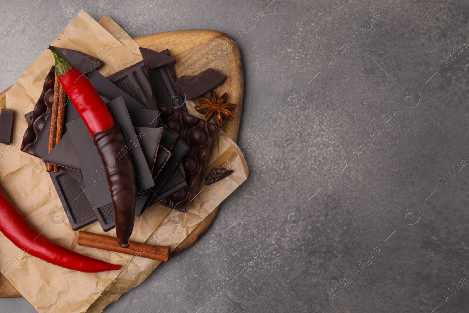 Photo of Red hot chili peppers and pieces of dark chocolate with spices on grey table, top view. Space for text