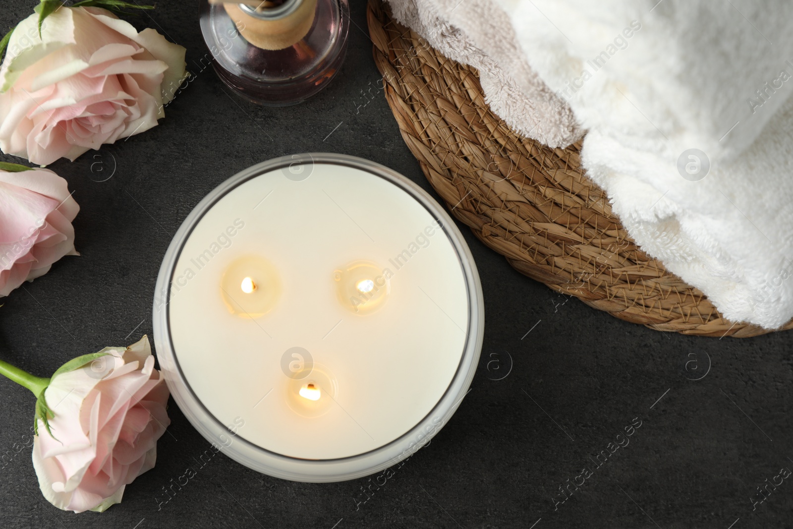 Photo of Spa composition with burning candle and rose flowers on grey table, flat lay