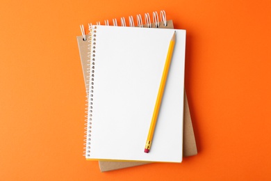 Notebooks with pencil on orange background, top view