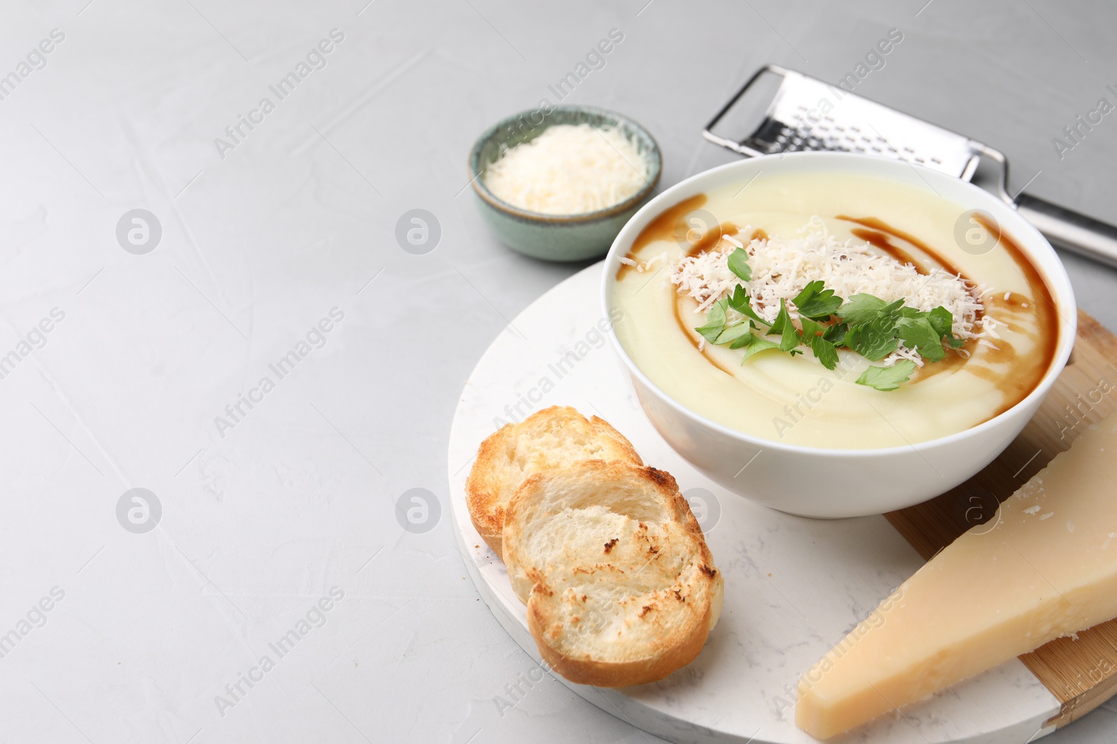 Photo of Delicious cream soup with parmesan cheese, soy sauce in bowl and croutons on light grey table. Space for text