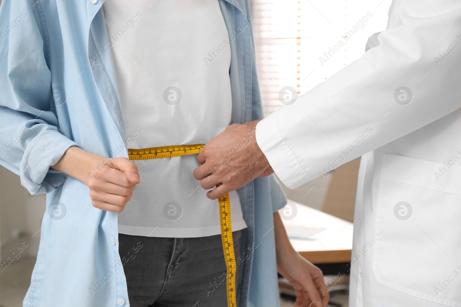 Photo of Nutritionist measuring young patient's waist in clinic, closeup