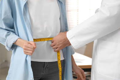 Nutritionist measuring young patient's waist in clinic, closeup