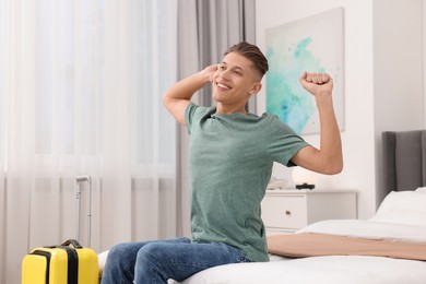 Smiling guest stretching on bed in stylish hotel room