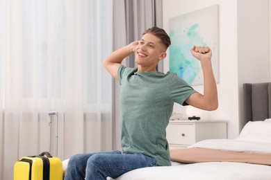 Photo of Smiling guest stretching on bed in stylish hotel room