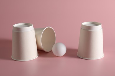 Photo of Shell game. Three paper cups and ball on pink background