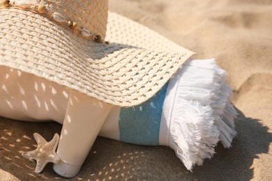 Straw hat, towel, sunscreen and starfish on sand, closeup
