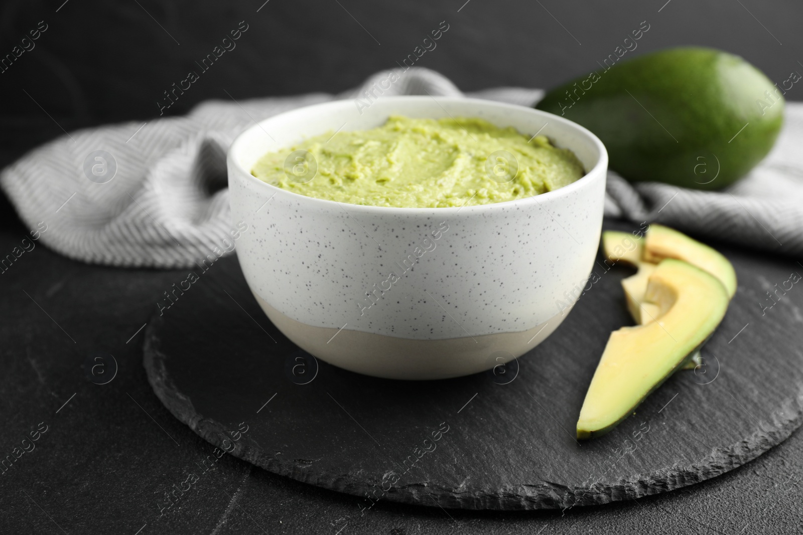 Photo of Bowl with guacamole made of ripe avocados served on black table