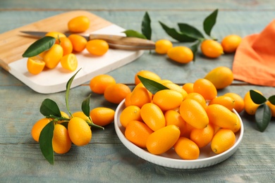 Photo of Fresh ripe kumquats and leaves on light blue wooden table