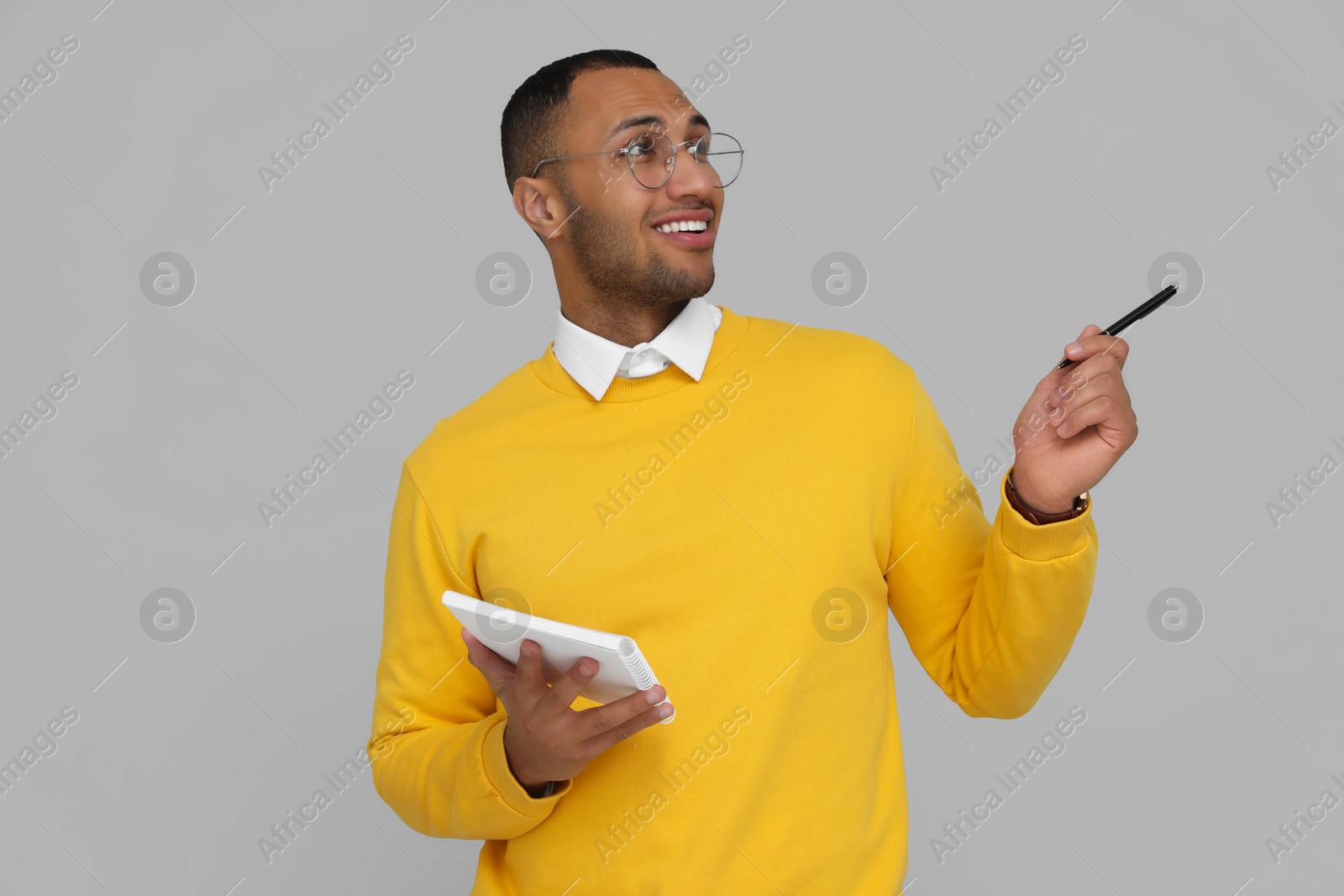 Photo of Happy young intern holding notebook and pen on light grey background