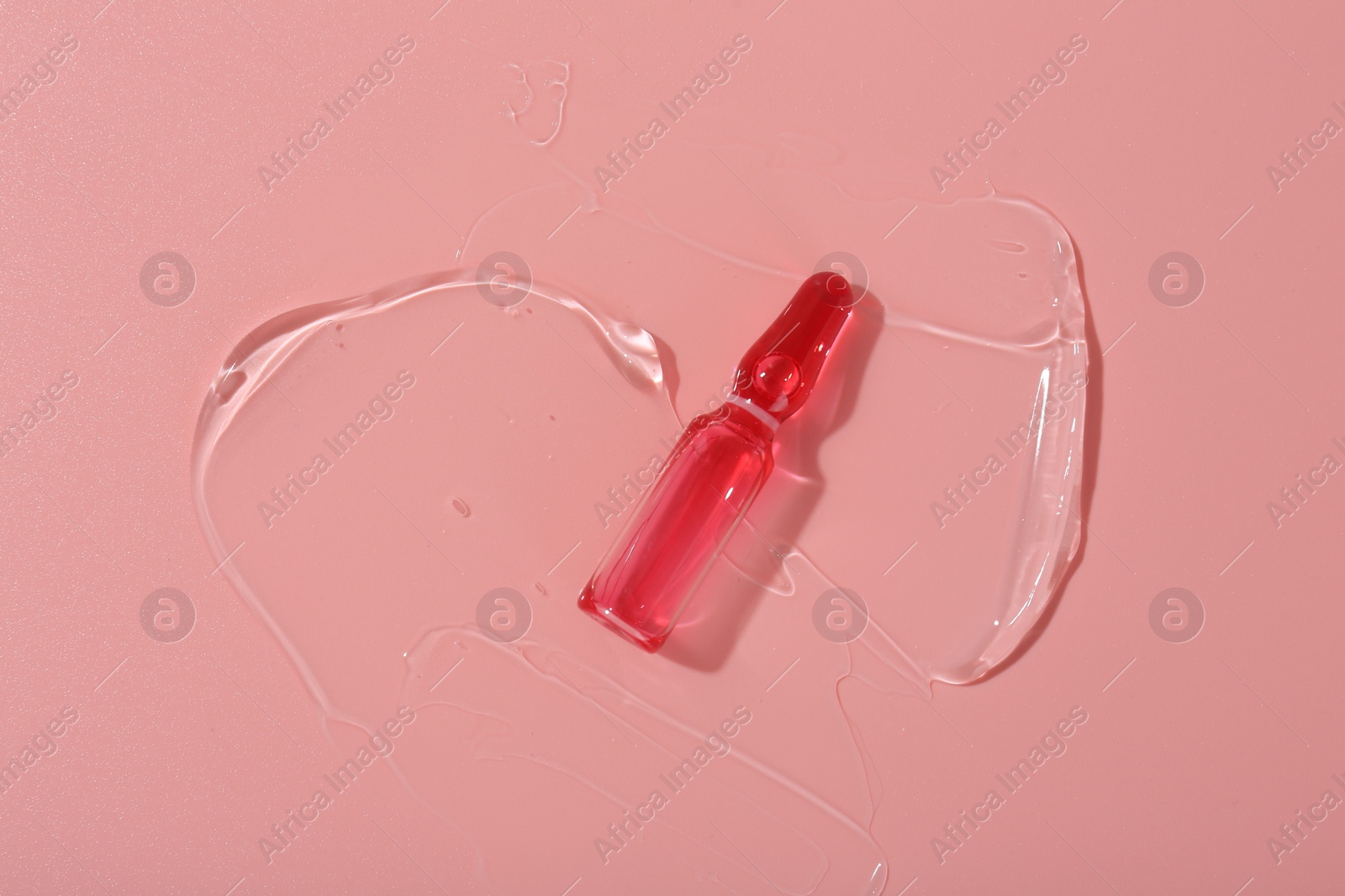 Photo of Skincare ampoule on pink surface with gel, top view