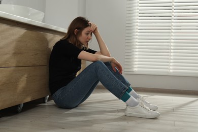 Photo of Sad young woman sitting on floor indoors