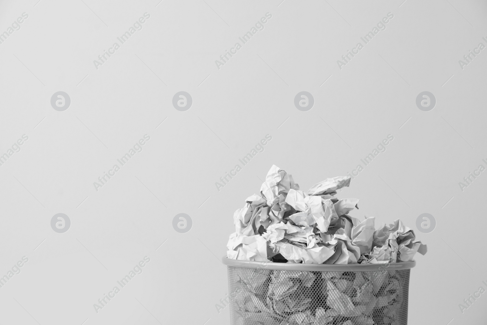 Photo of Metal bin with crumpled paper against light background, space for text