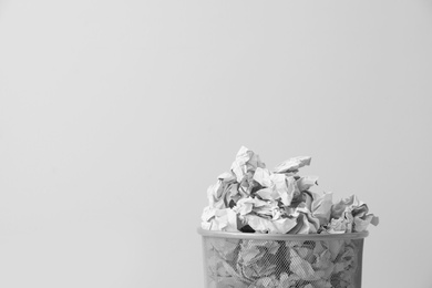 Photo of Metal bin with crumpled paper against light background, space for text