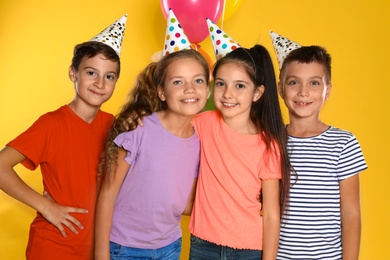 Photo of Happy children in party hats on yellow background. Birthday celebration