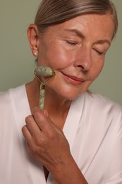 Photo of Woman massaging her face with jade roller on green background