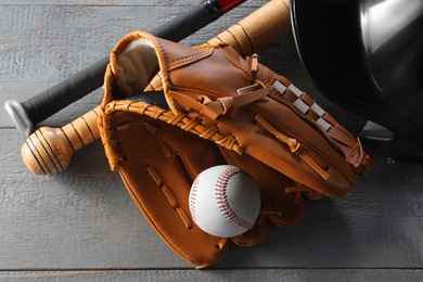 Photo of Baseball glove, bats, ball and batting helmet on grey wooden table, closeup