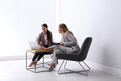 Young businesswomen sitting in armchairs at table indoors