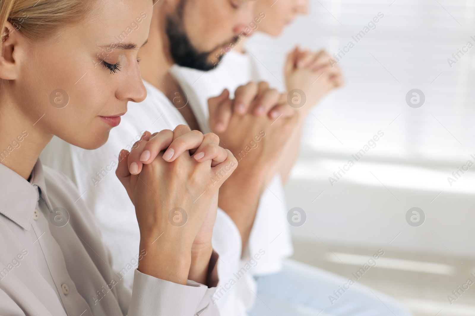 Photo of Young woman praying among other religious people indoors. Space for text