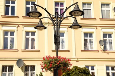 Photo of Street lamp with beautiful blooming flowers in front building outdoors
