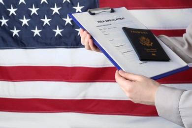 Photo of Woman holding visa application form and passport against American flag, closeup. Space for text