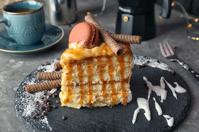 Photo of Piece of delicious homemade cake with caramel sauce and macaron on table