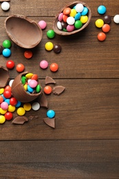 Photo of Broken chocolate eggs and colorful candies on wooden table, flat lay. Space for text