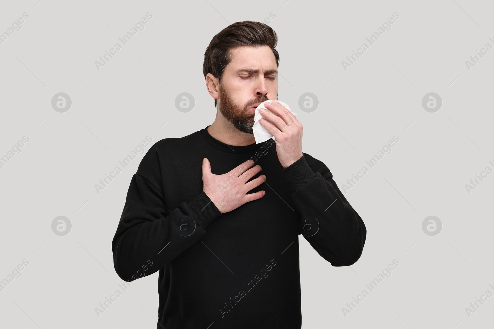 Photo of Sick man with tissue coughing on light grey background