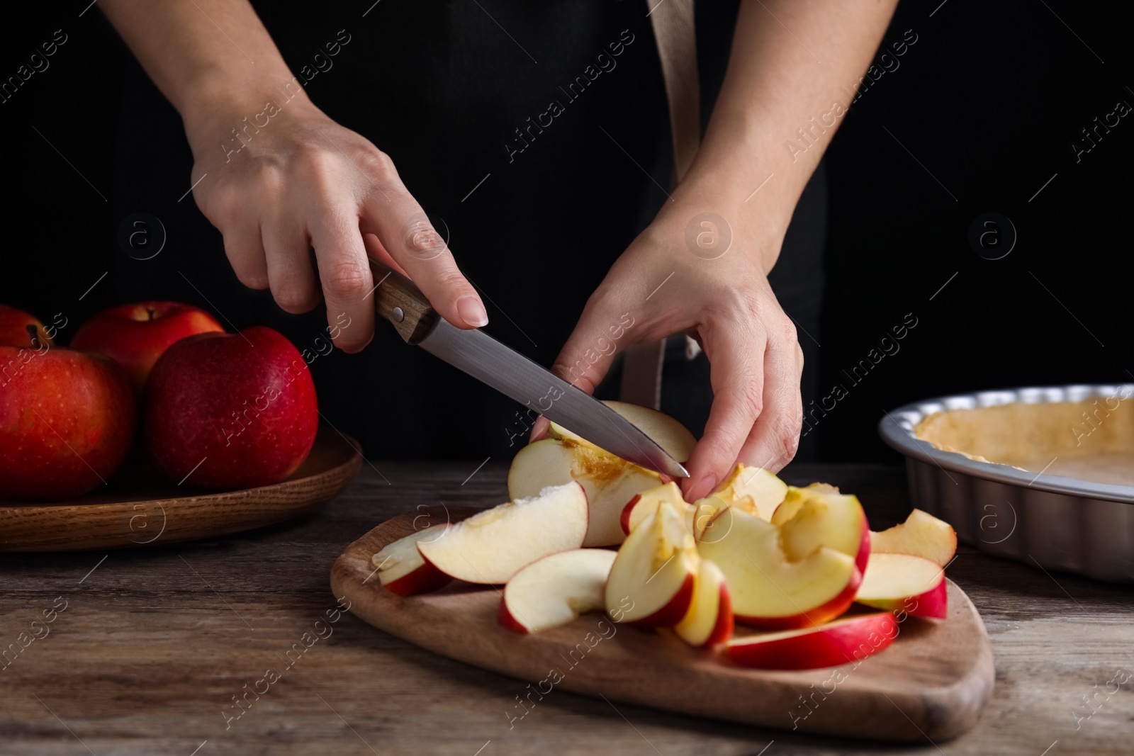 Photo of Woman cutting apple to make traditional English pie at wooden table, closeup
