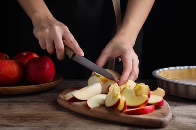 Woman cutting apple to make traditional English pie at wooden table, closeup