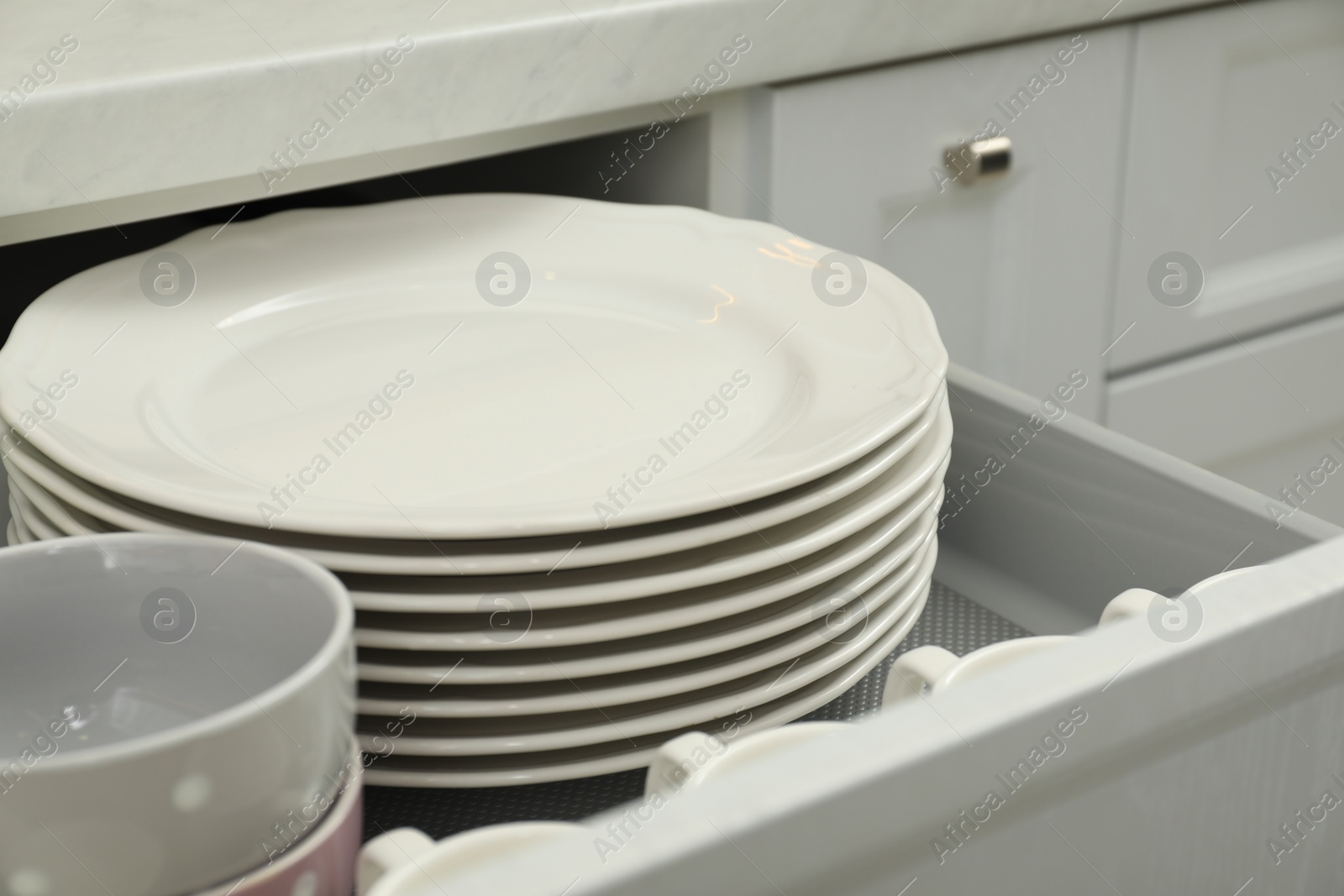 Photo of Clean plates and bowls in drawer indoors, closeup