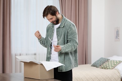 Photo of Happy man opening parcel at home. Internet shopping