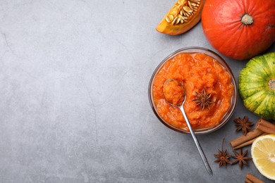 Bowl of delicious pumpkin jam and ingredients on grey table, flat lay. Space for text