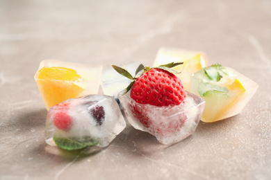 Ice cubes with different berries and mint on grey table, closeup