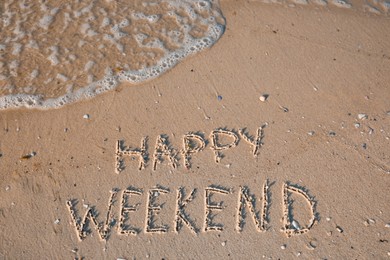 Photo of Phrase Happy weekend written on sand at beach, top view