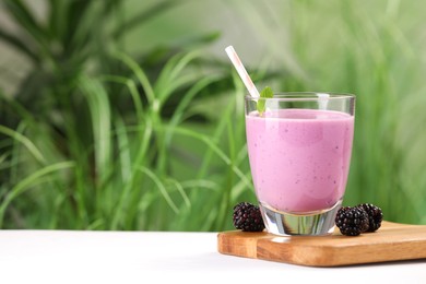 Photo of Delicious blackberry smoothie in glass and berries on white table, space for text