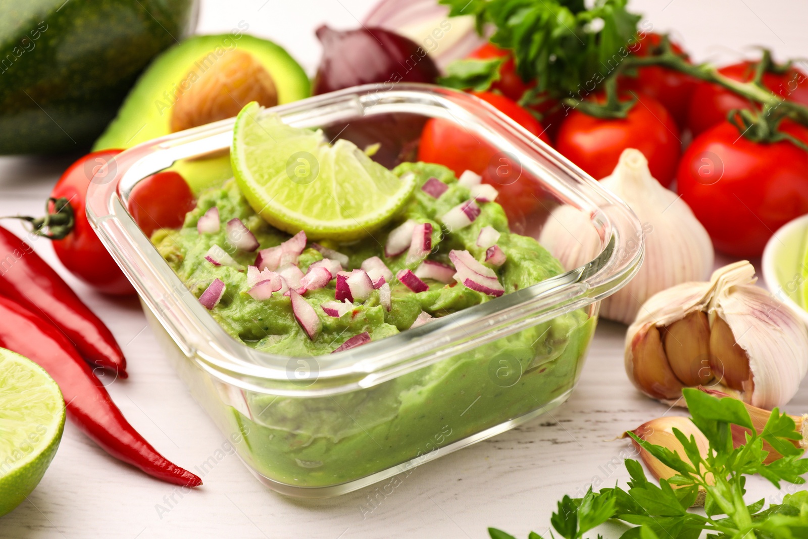 Photo of Bowl of delicious guacamole with onion, lime and ingredients on white wooden table, closeup